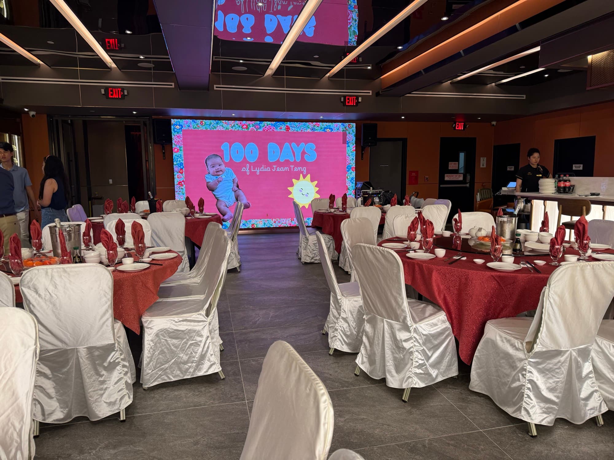 Banquet hall set with red and white linens beneath the LED screen