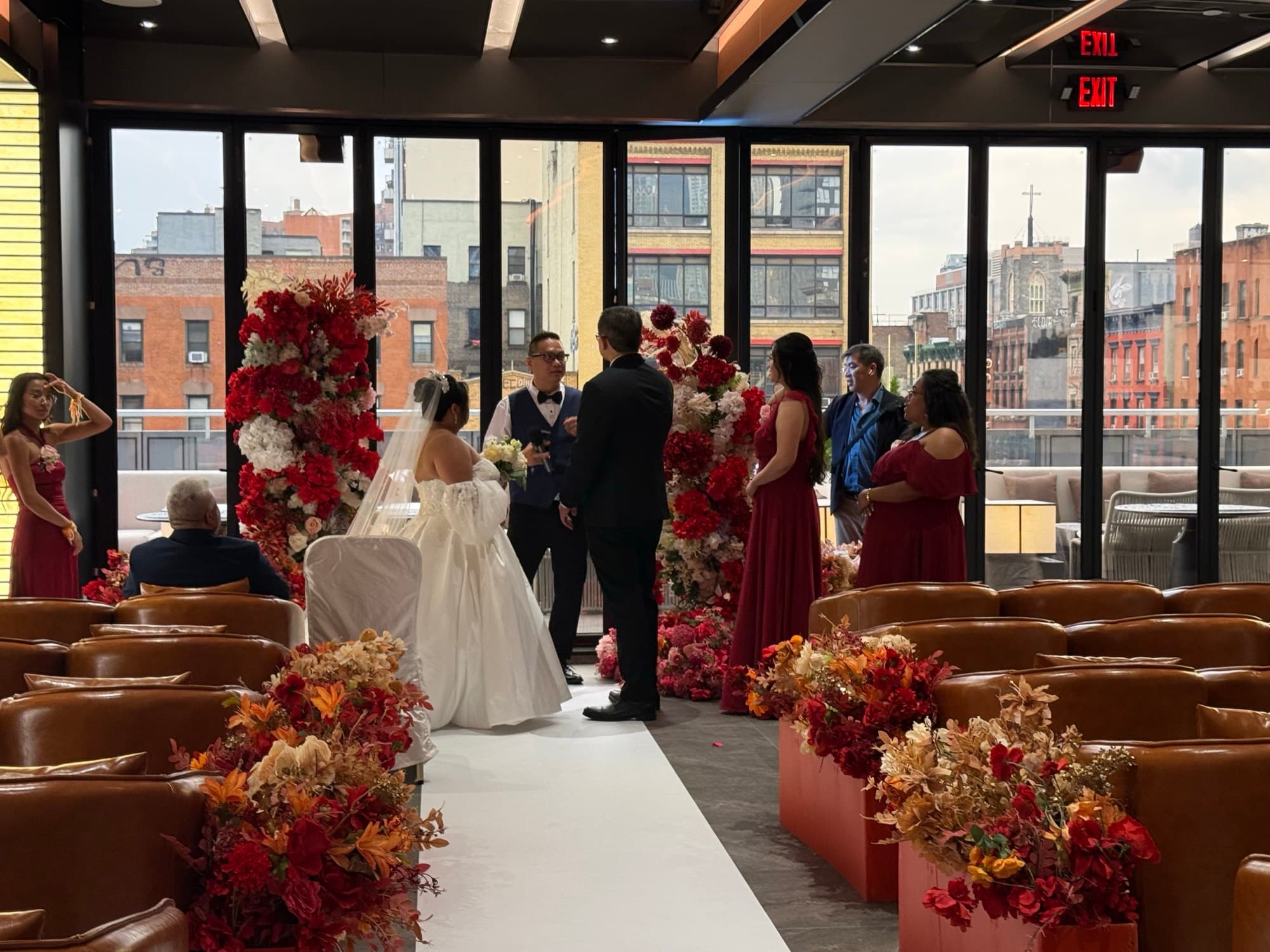 A couple at a floral ceremony backdrop by the city windows