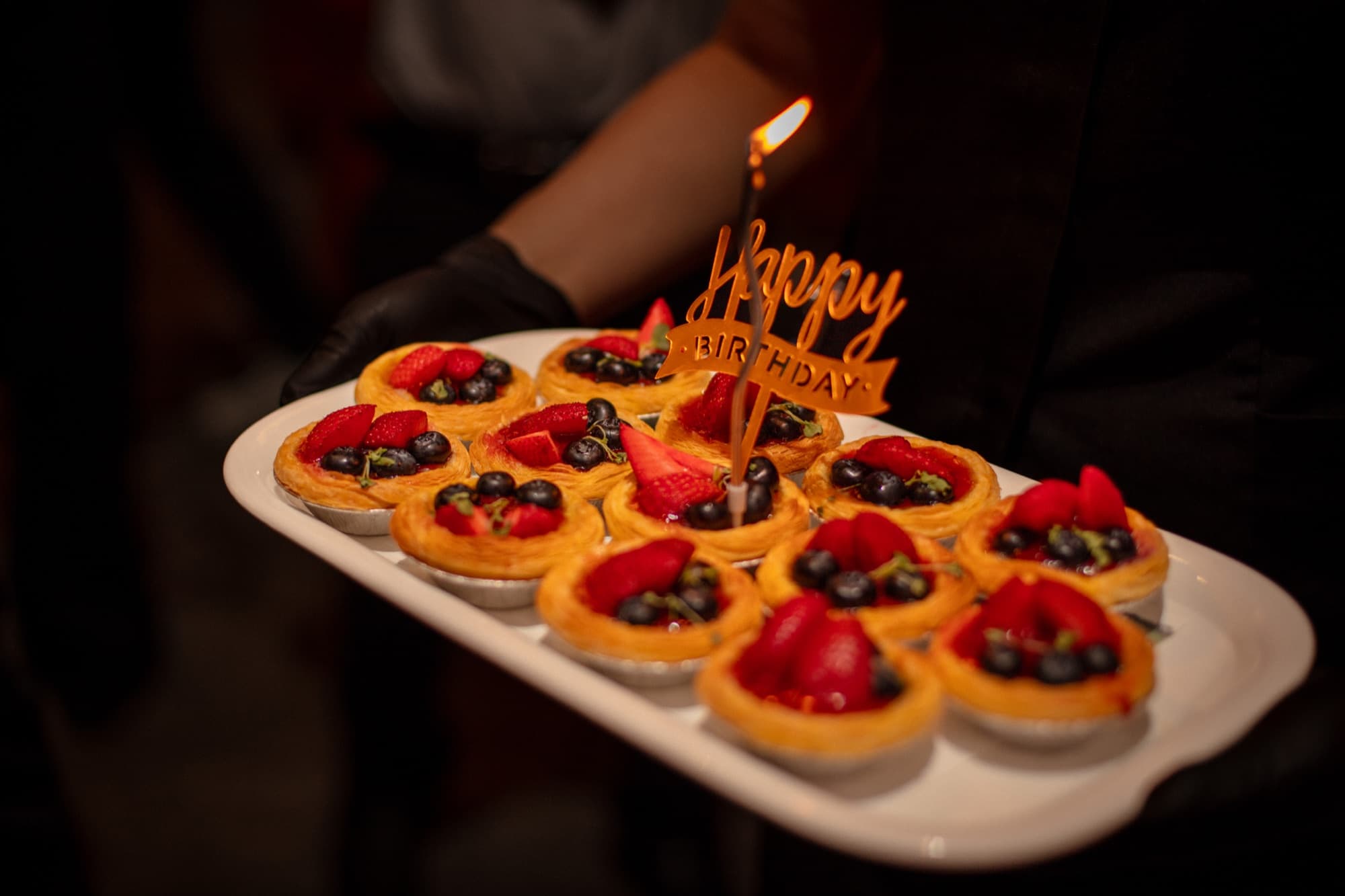 A tray of fruit tarts carried out with a Happy Birthday candle