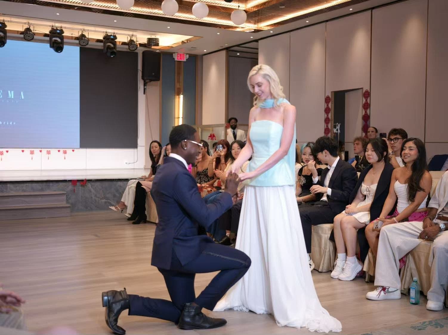 A staged proposal moment on the runway in front of the seated house