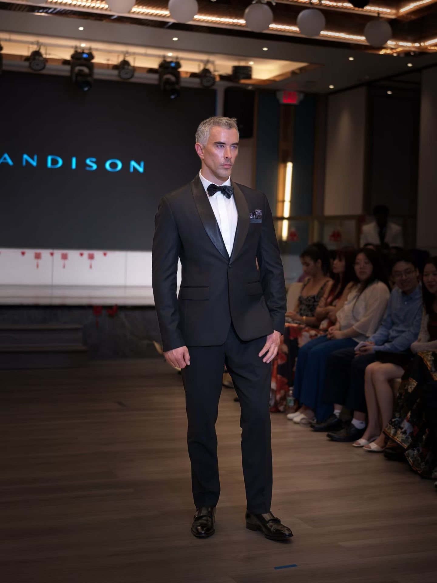 A model in a black tuxedo at the end of the runway